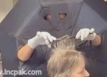 Hairdresser uses an umbrella to keep a distance from her clients